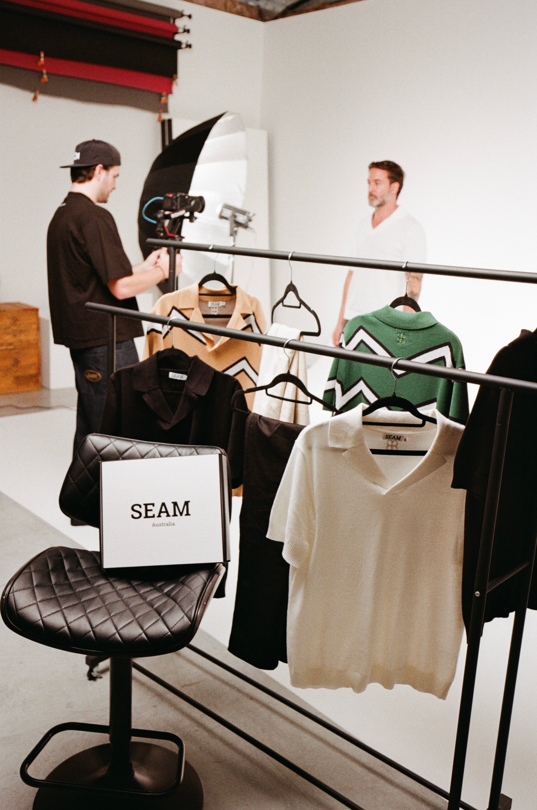 Man filming another man in a clothing store with 'SEAM' branding.