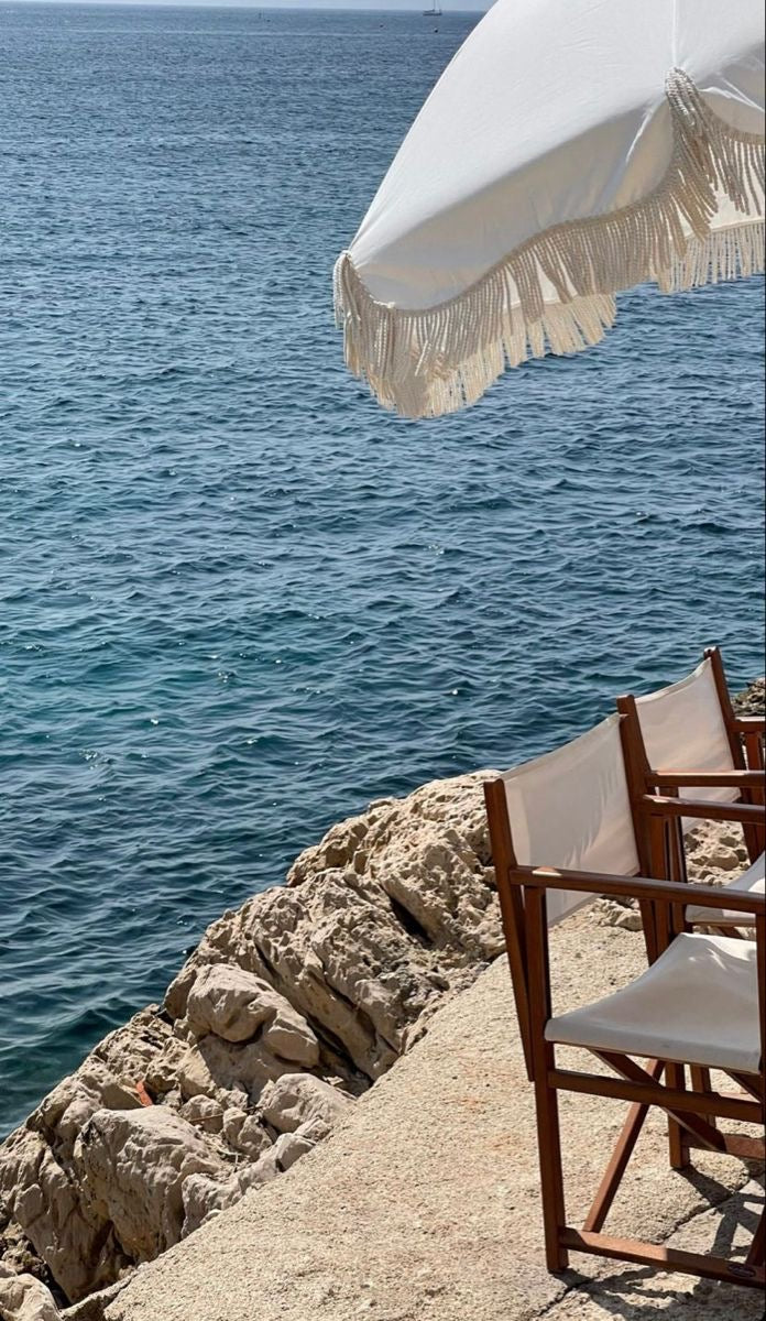 White umbrella and chairs by the ocean on a rocky shore