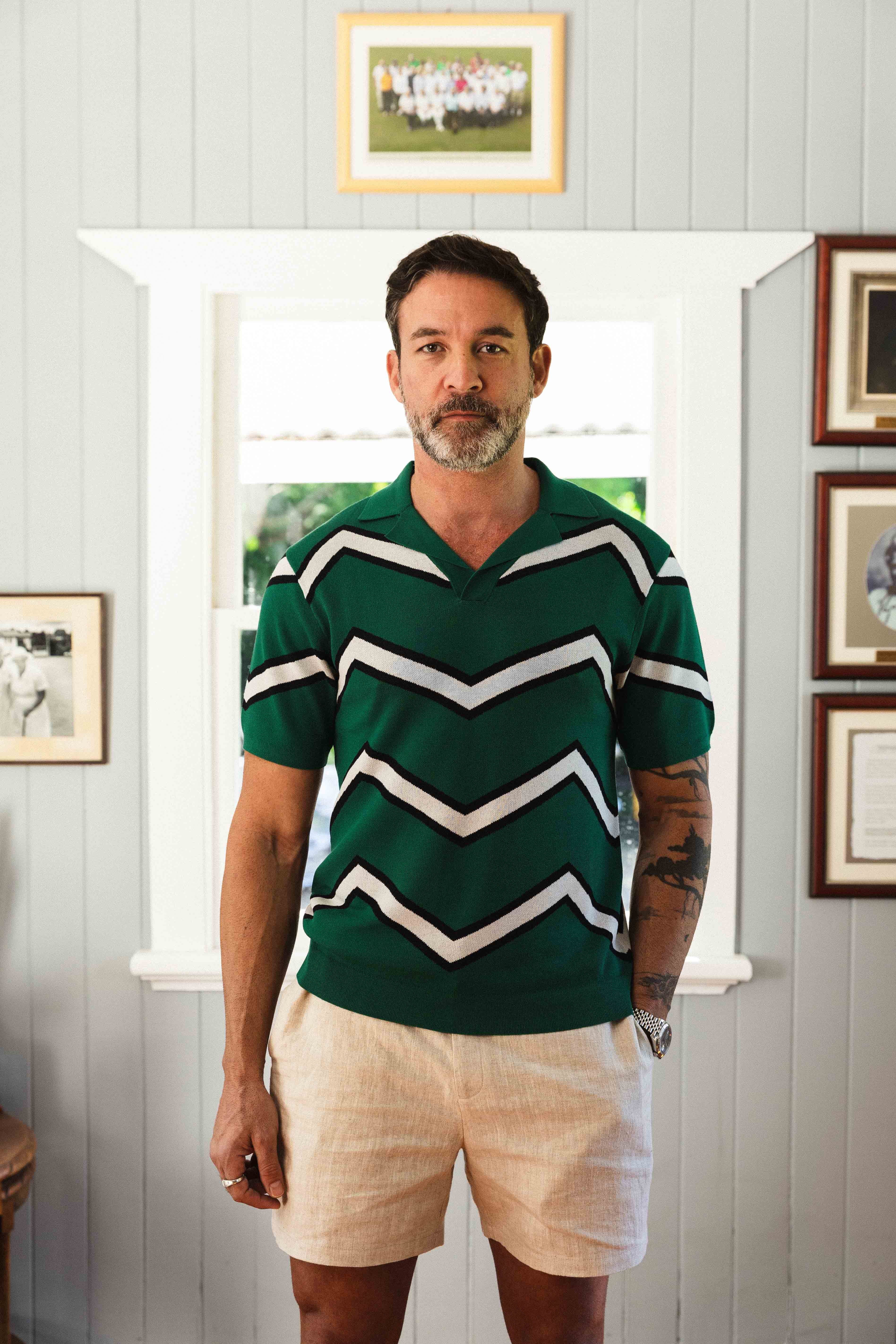 Man wearing a green rugby jersey with white stripes in a room with framed pictures on the wall.