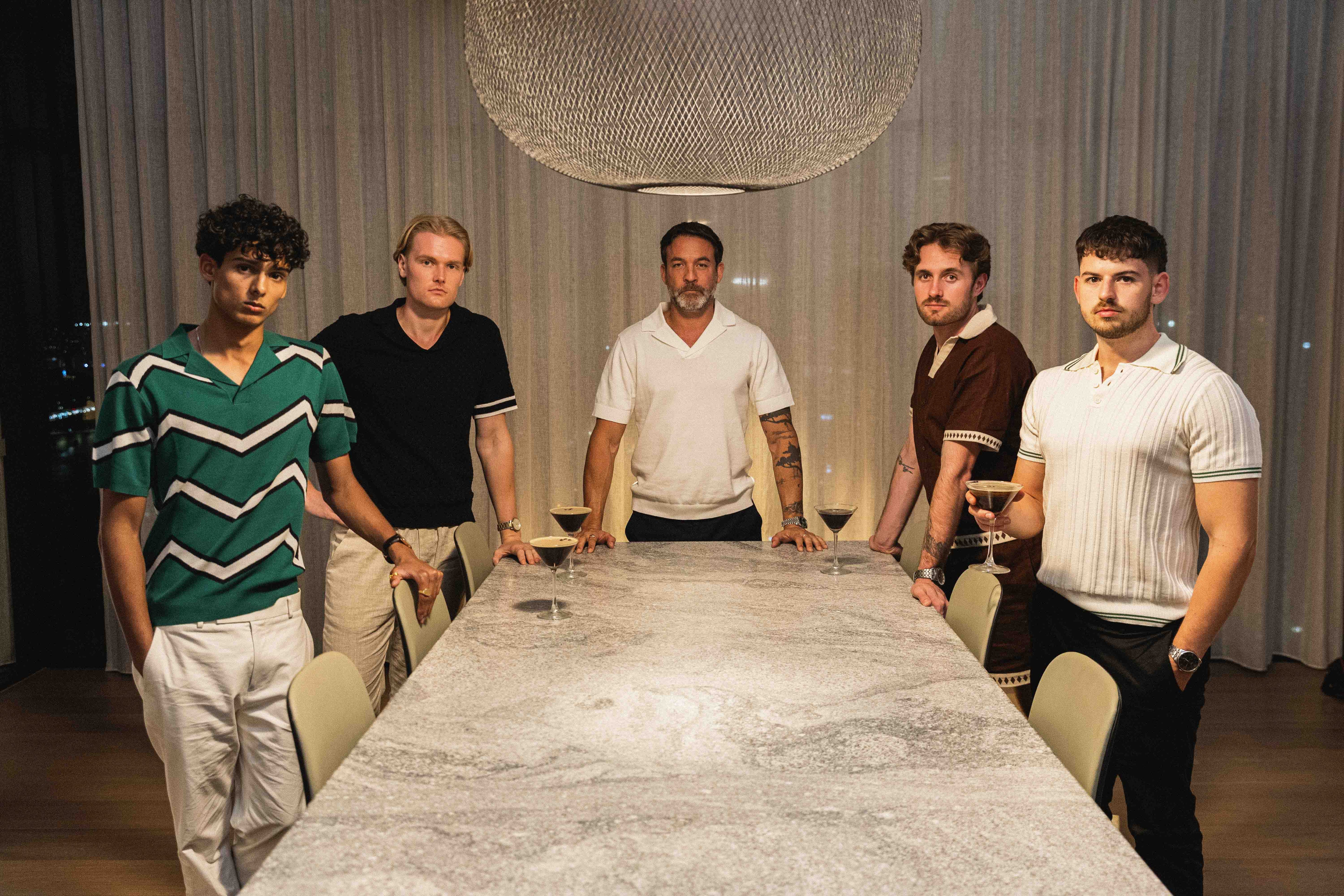 Five men standing around a marble table in an indoor setting.