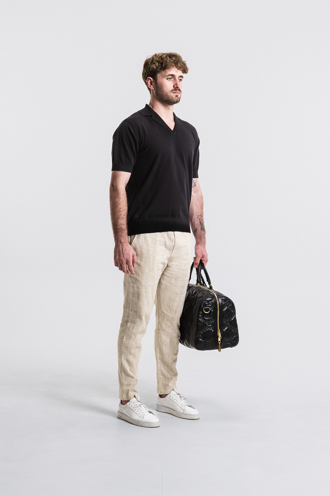 SEAM Cotton Knit Open Neck Polo in Black, model styled with duffel bag and linen pants