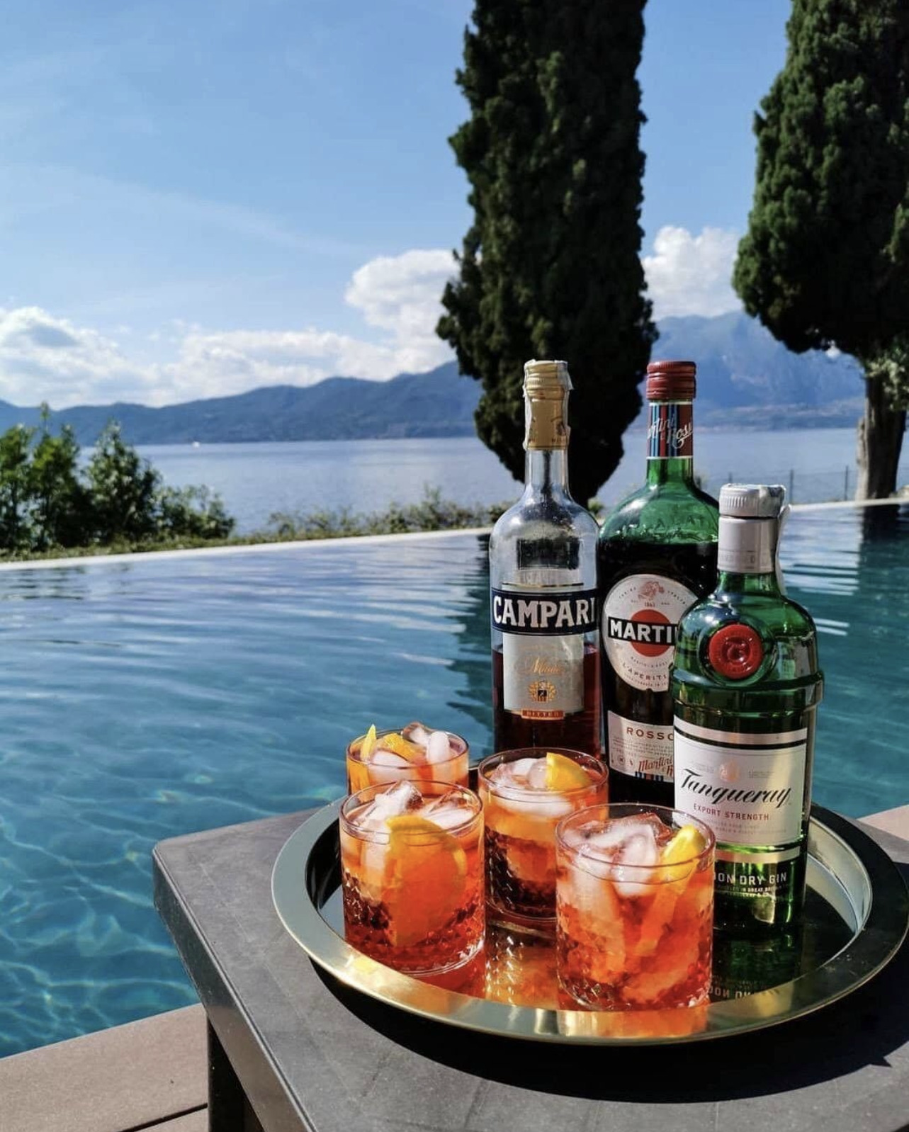 Tray with cocktails and alcohol bottles by a poolside with scenic background