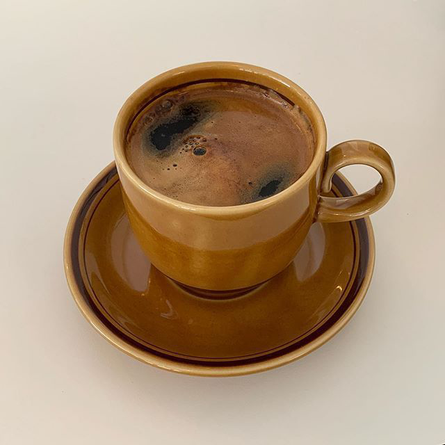 Brown ceramic cup and saucer with coffee on a beige background