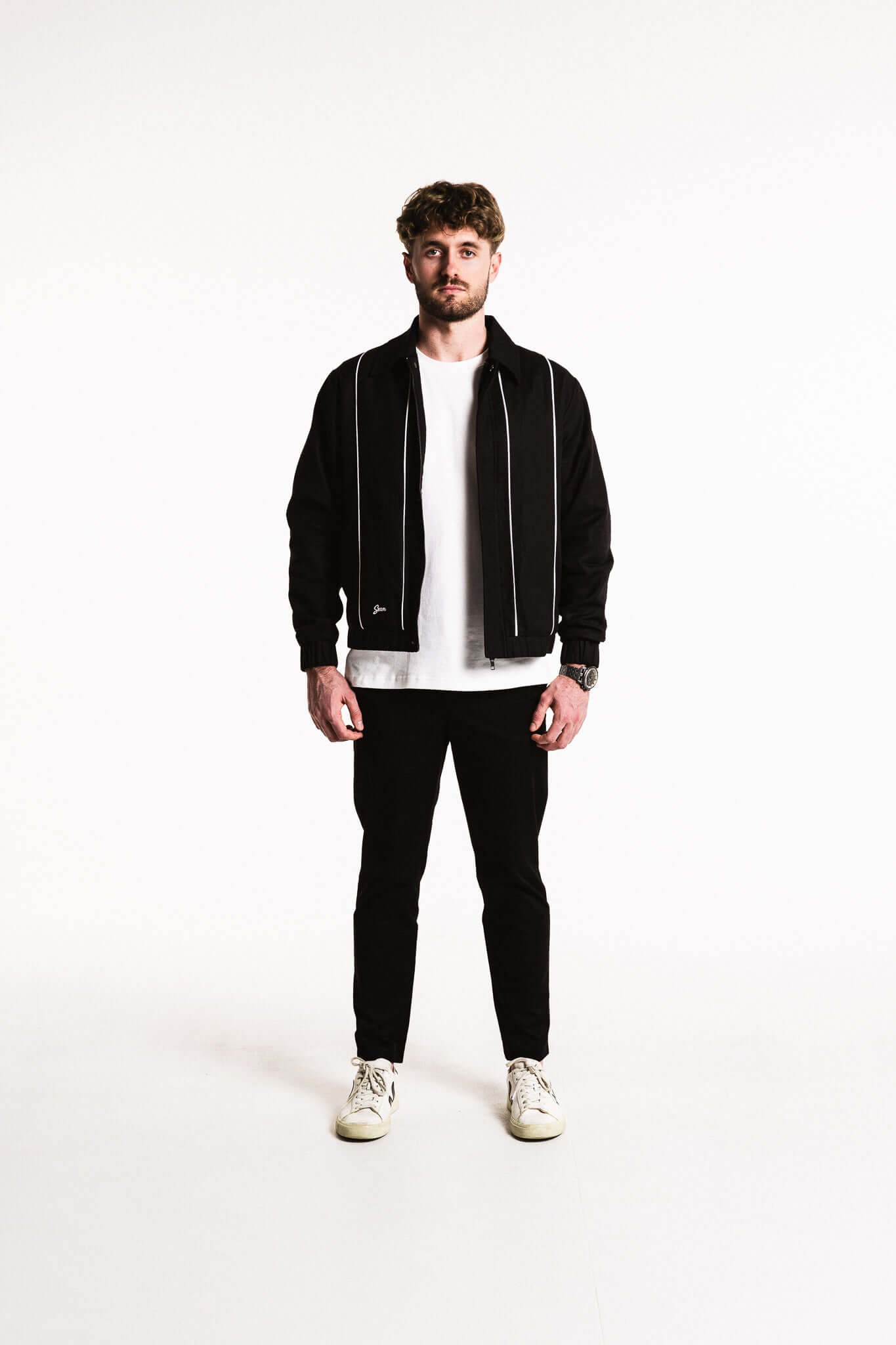 A model wearing a Cotton Contrast Jacket with contrasting white piping and elasticated cuffs, paired with black pants.